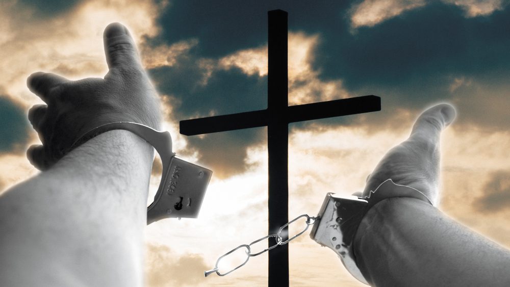 An image of the cross with broken chains of a prisoner in the foreground.